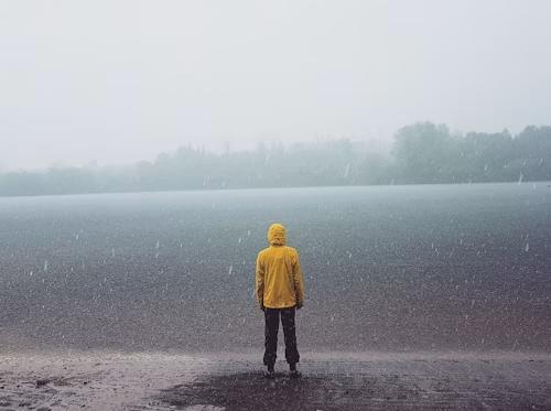 Person standing in heavy rain wearing a yellow waterproof jacket | Dwights NZ